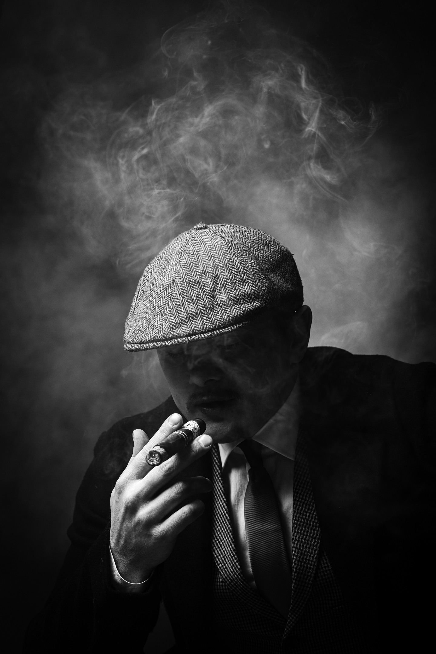 Black and white studio character portrait, man in flat cap smoking a cigar